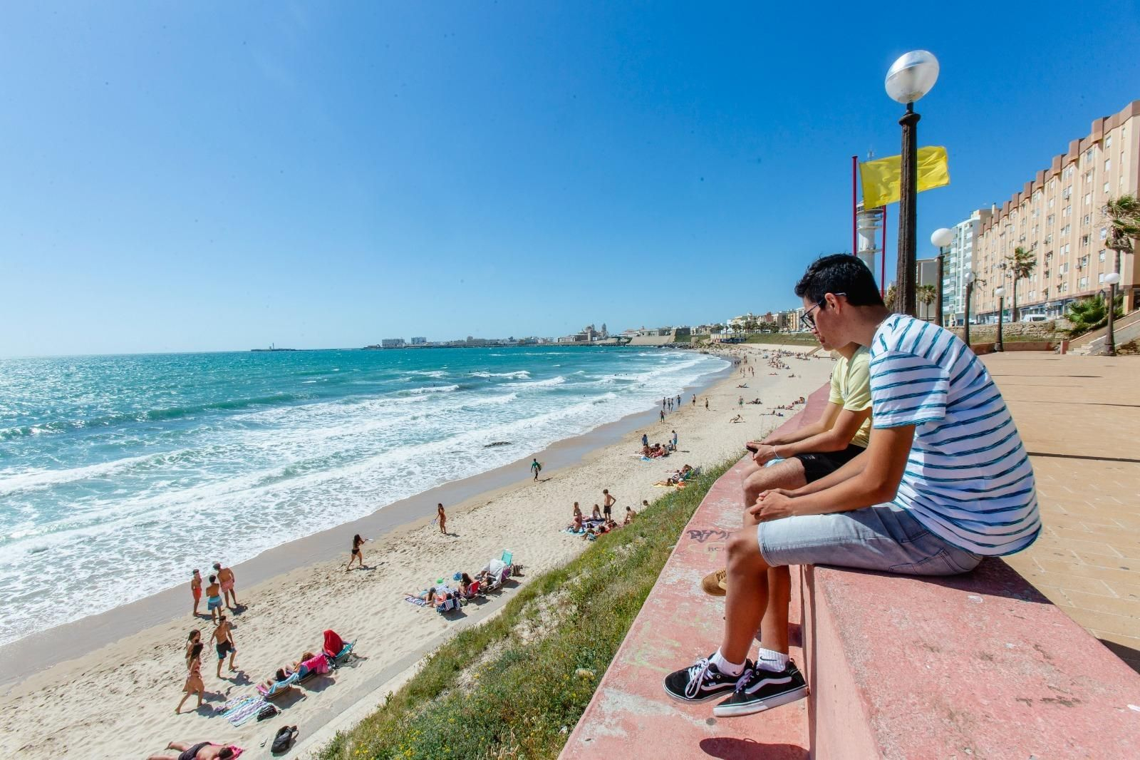 Dos jóvenes observan la playa de Santa María del Mar, con bandera amarilla.