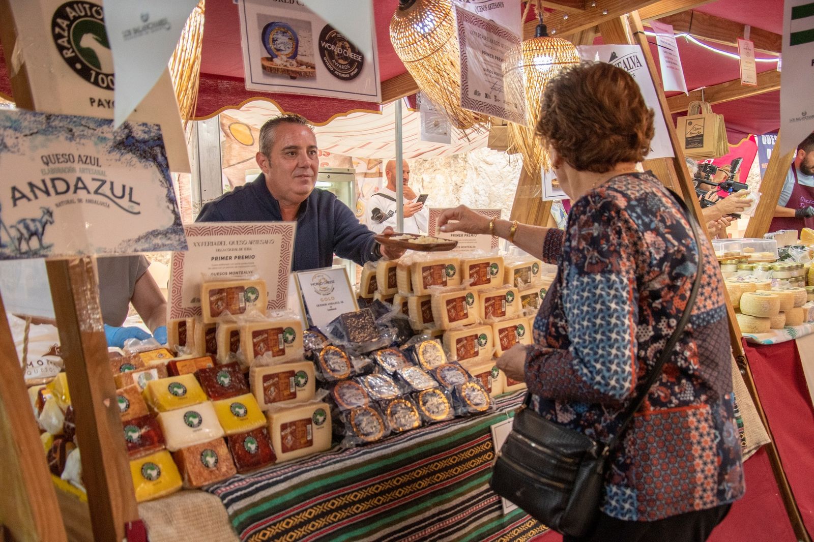 Uno de los expositores de la Feria del Queso de Zuheros ofrece queso a una señora.