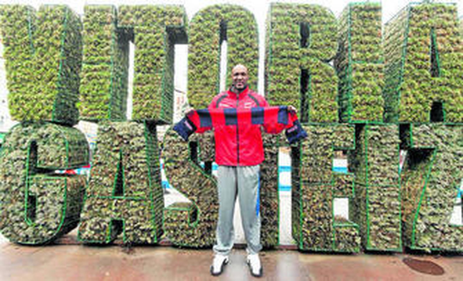 Lamar Odom posa con una bufanda baskonista a su llegada a Vitoria con el nombre de la ciudad a su espalda.