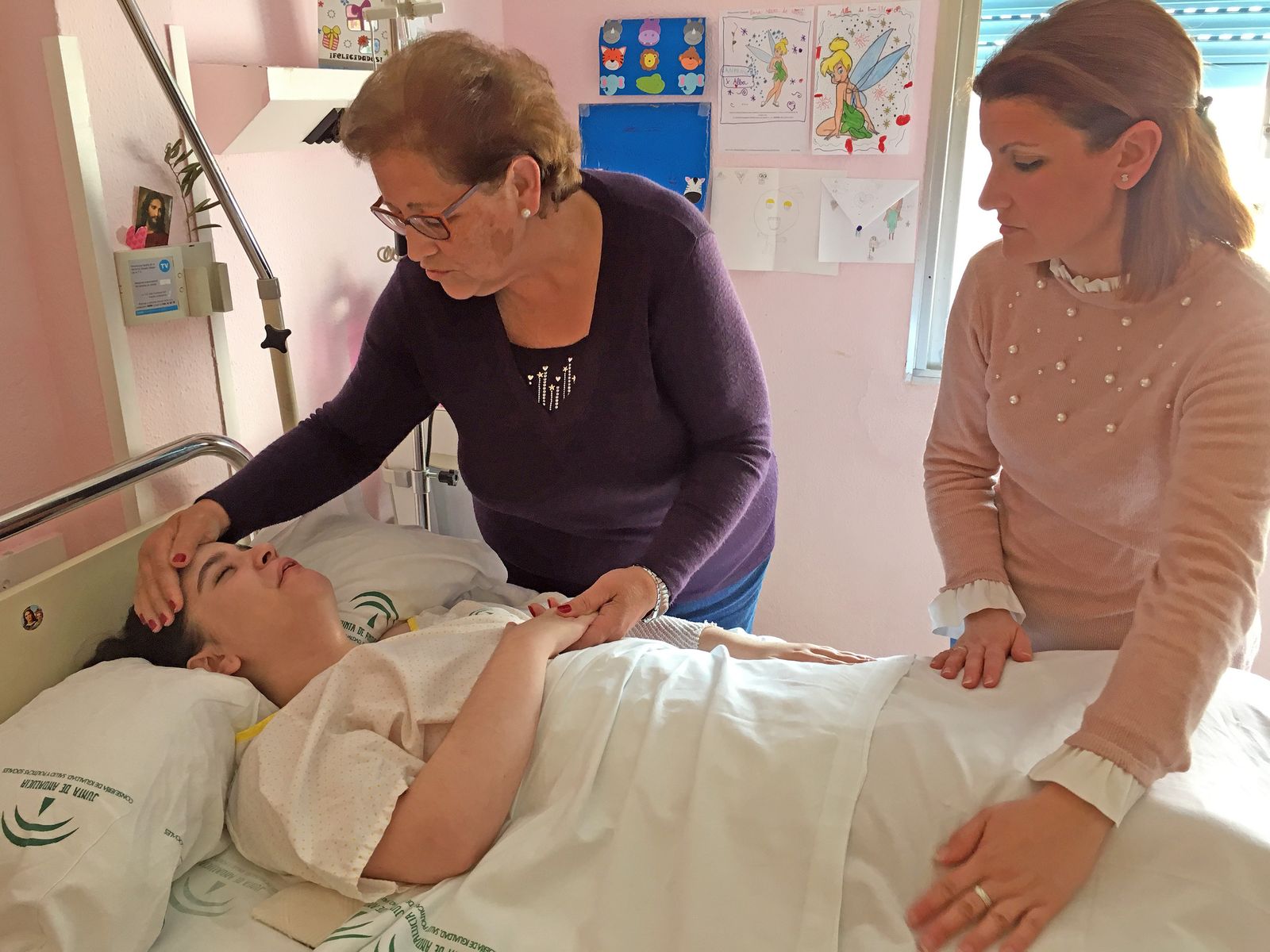 Alba, en la cama del hospital, es atendida por su madre y su tía.