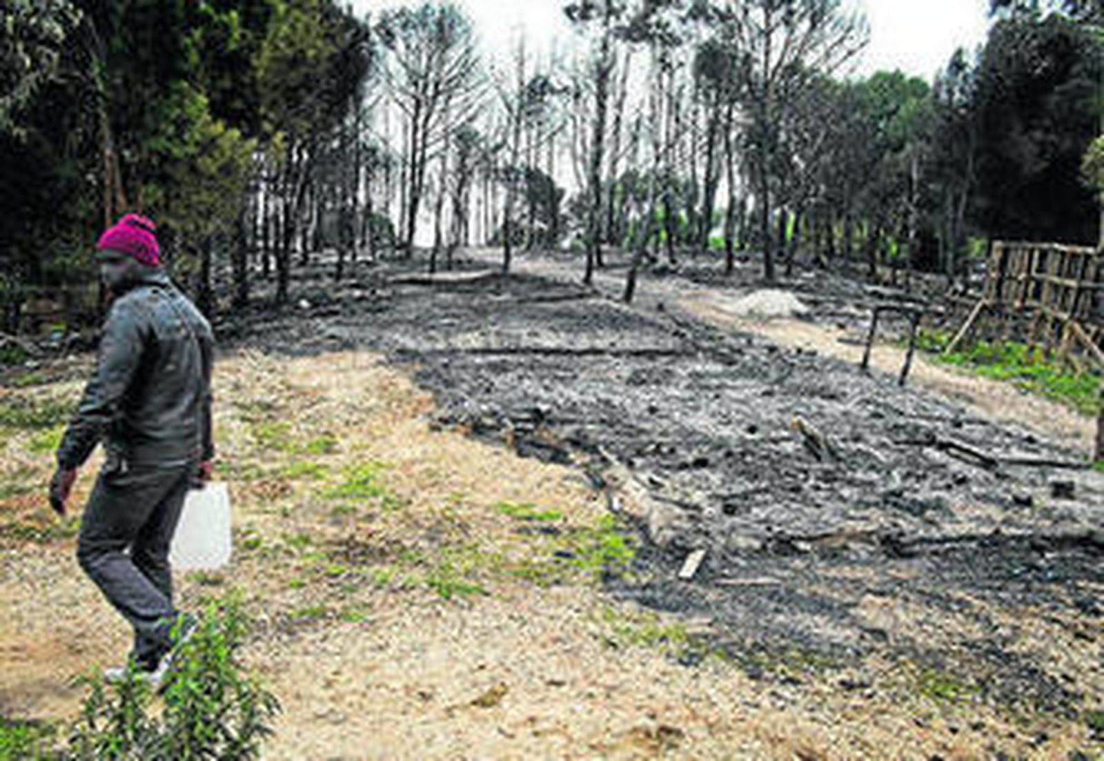 Un inmigrante camina, ayer, entre los restos calcinados del asentamiento de Palos (Huelva).