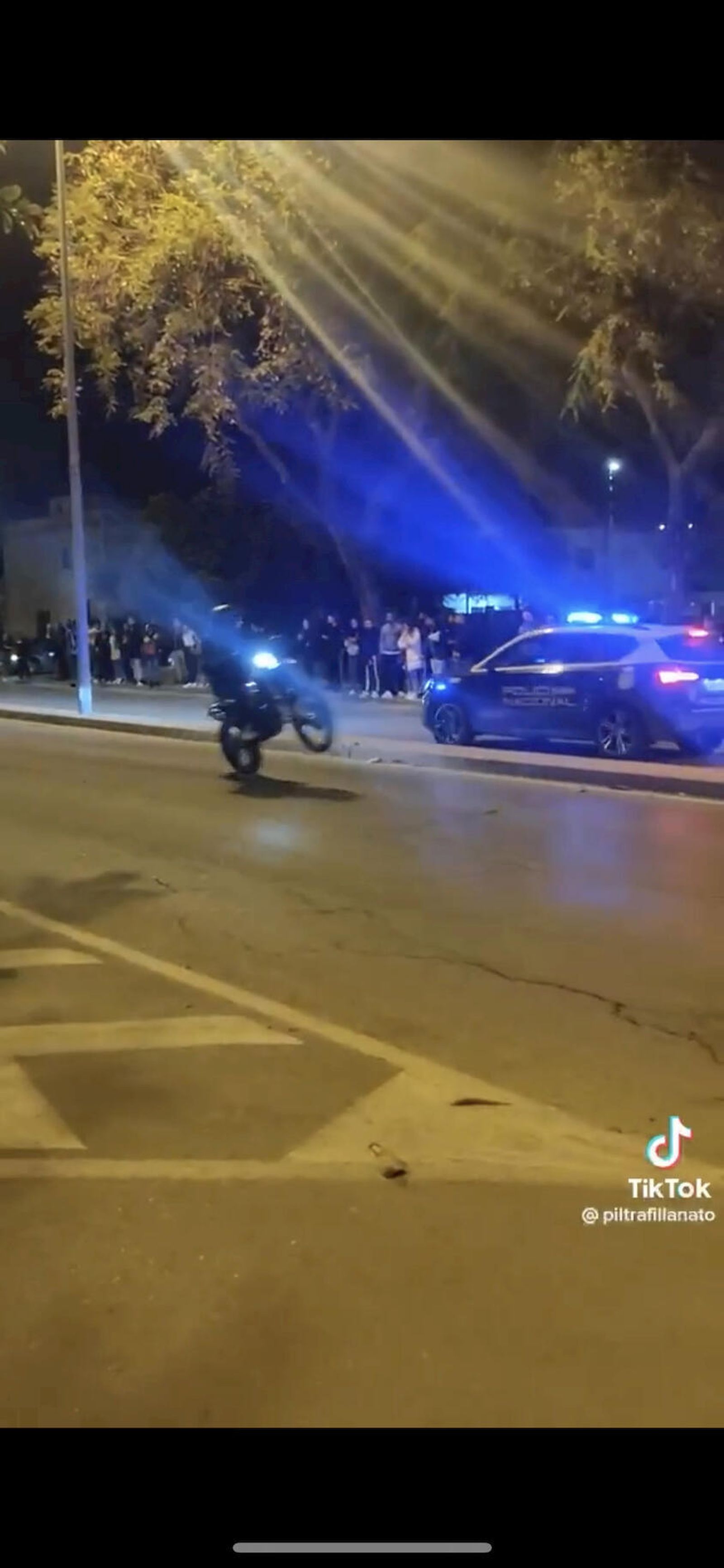 Un motorista hace un 'caballito' junto a un coche de la Policía Nacional.