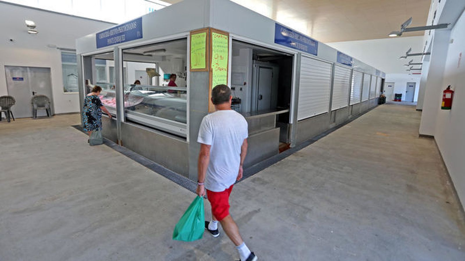 Imagen de una de las entradas al mercado en la que se observa a un cliente con una bolsa de la compra y a otra comprando en un puesto.