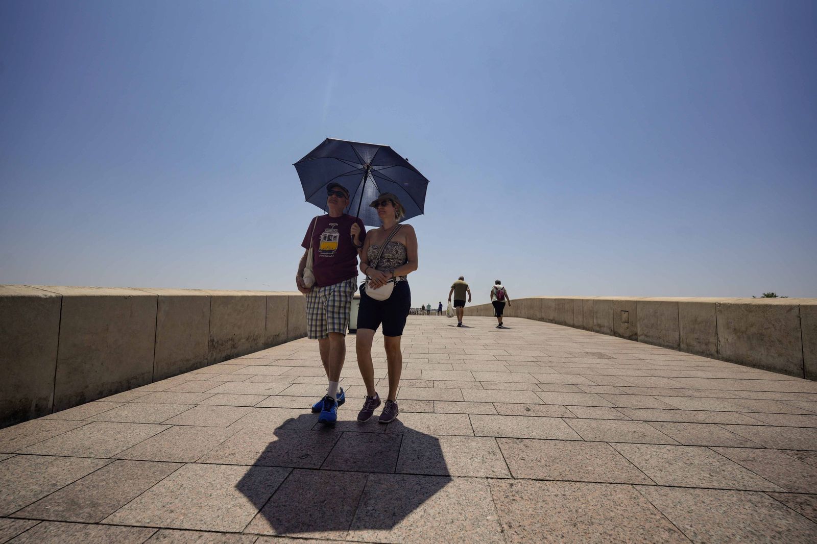 Dos personas pasan por el Puente Romano de Córdoba bajo un paraguas para resguardarse del sol.
