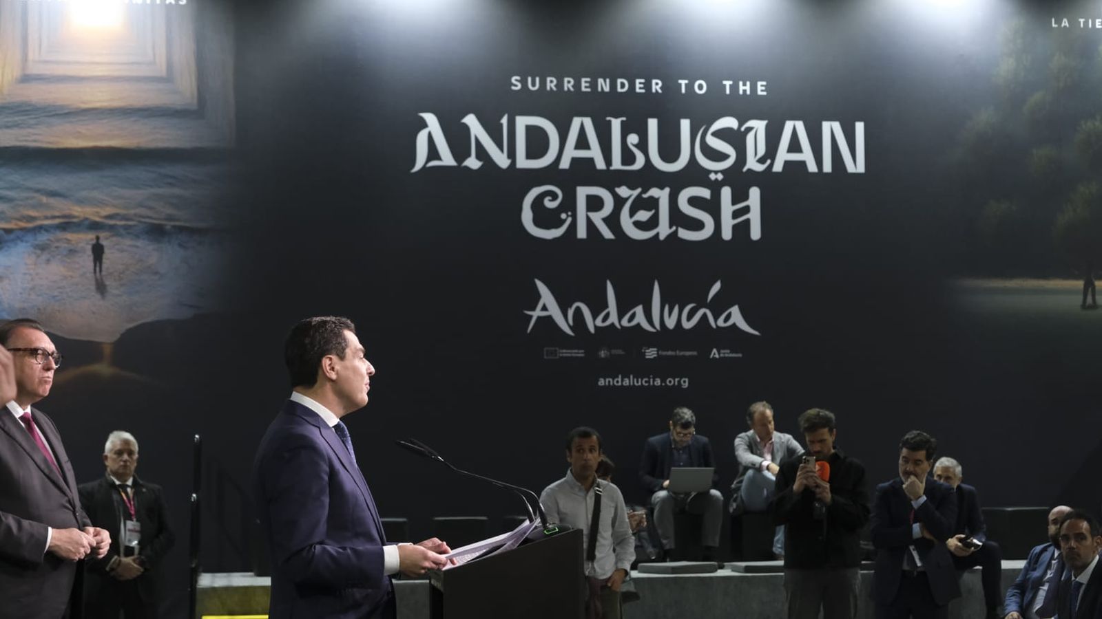 Juanma Moreno, con el panel de fondo con el lema de la campaña andaluza 'Surrender to the Andalusian Crush'.