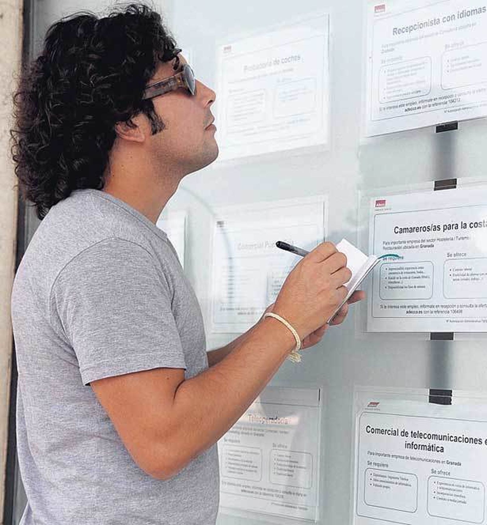 Un joven consulta ofertas laborales en el escaparate de una ETT. / D. S.