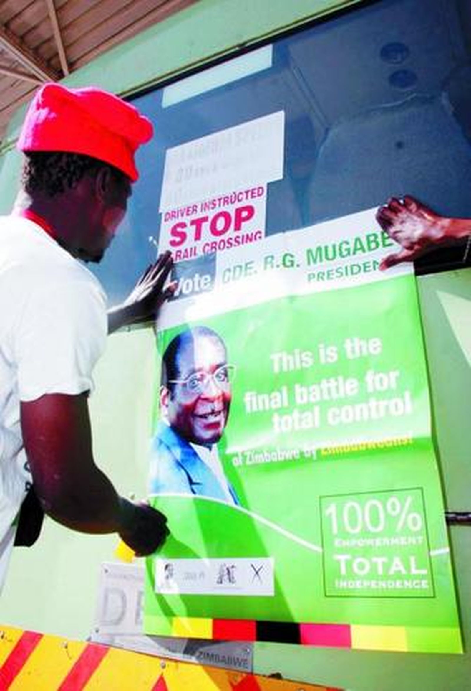 Un zimbabuense pega un cartel electoral a favor del presidente, Robert Mugabe.