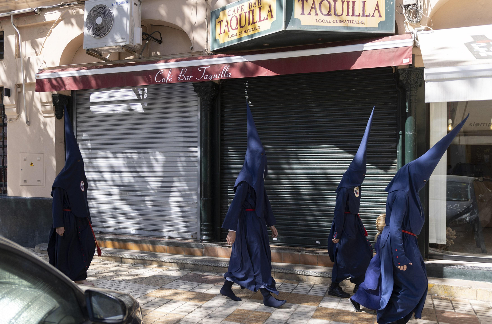 Nazarenos del Baratillo pasan por delante del bar Taquilla, cerrado este Miércoles Santo.