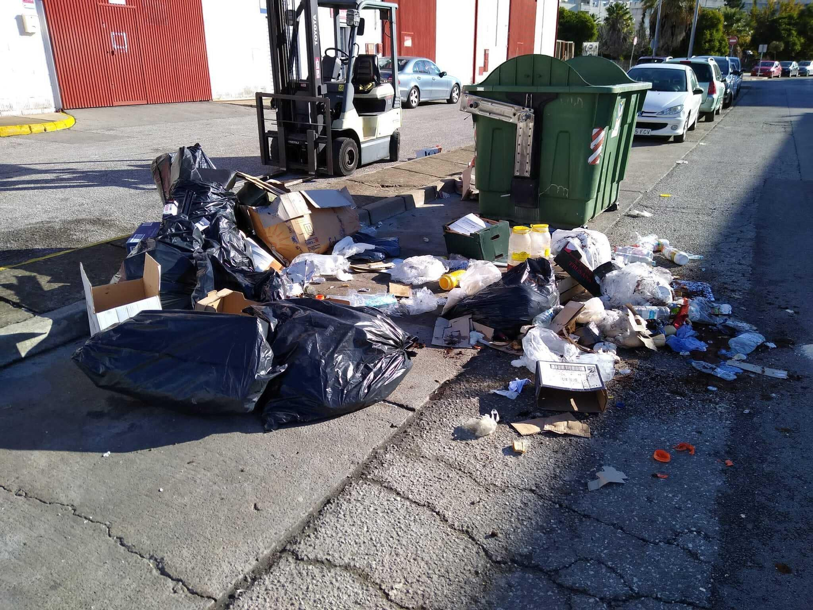 Basura acumulada sin recoger junto a un contenedor.
