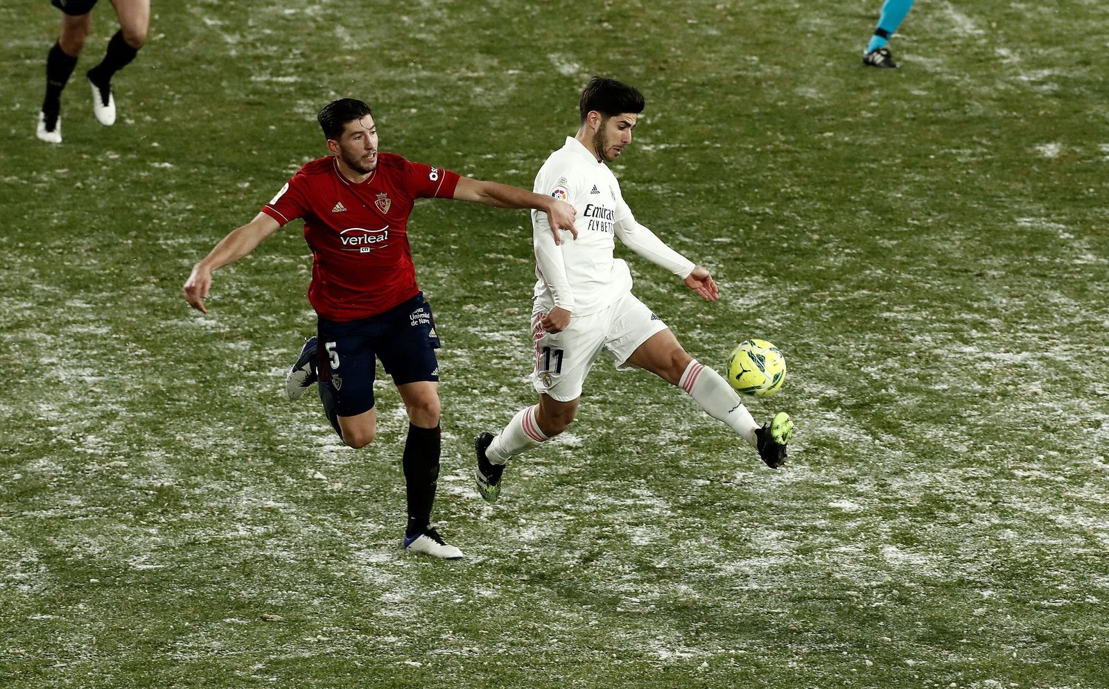 Marco Asensio golpea el balón ante David García con los restos evidentes de la nieve sobre el césped de El Sadar.
