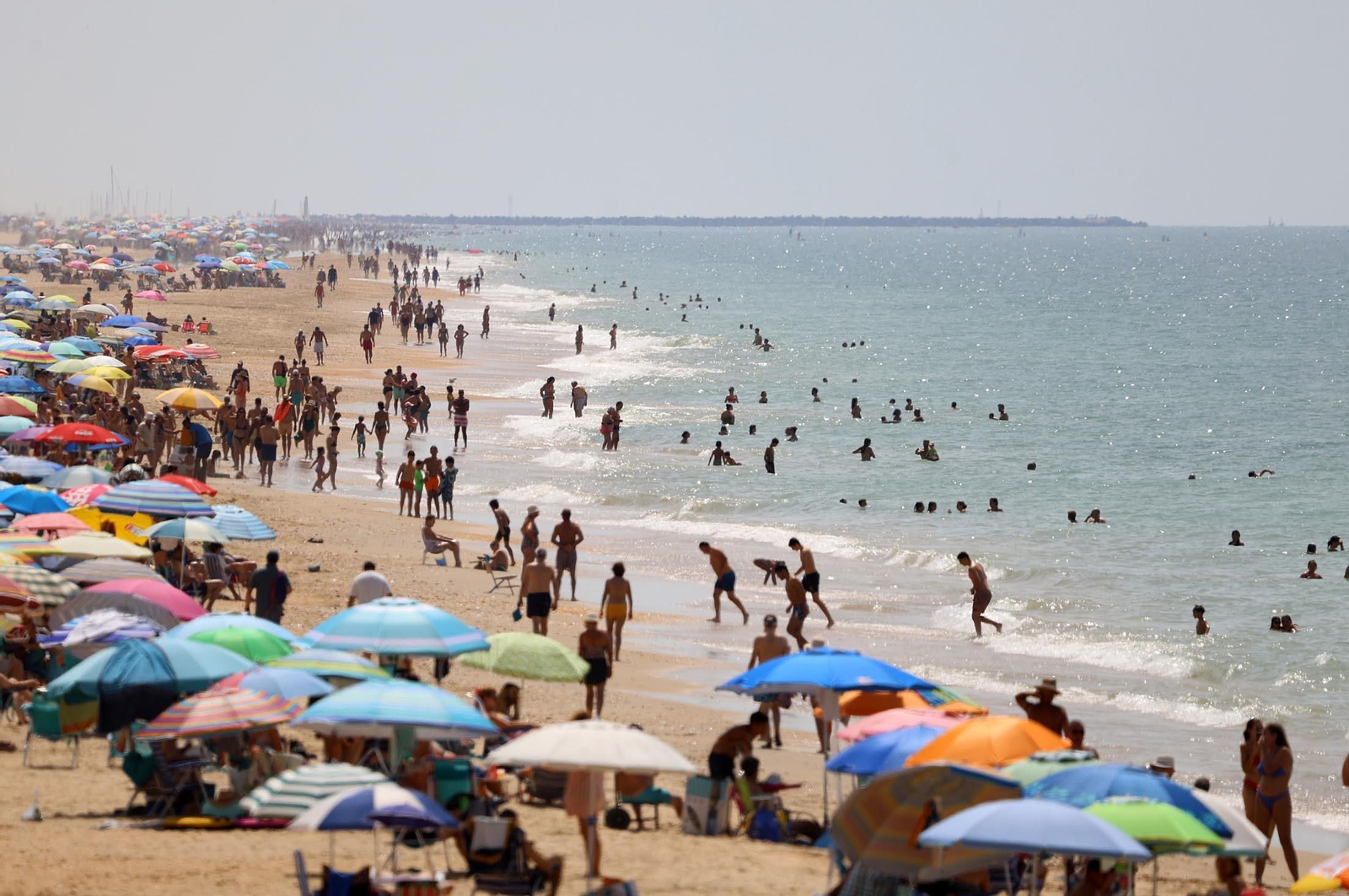 Aspecto de una de las playas españolas con varias personas introducidas en el mar durante un día del presente verano.