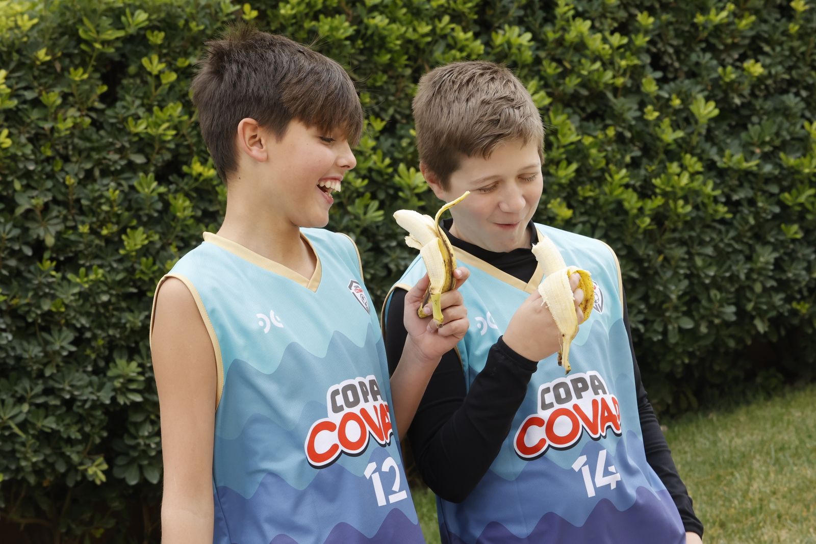 Dos niños participantes en la Copa Covap se comen un plátano.