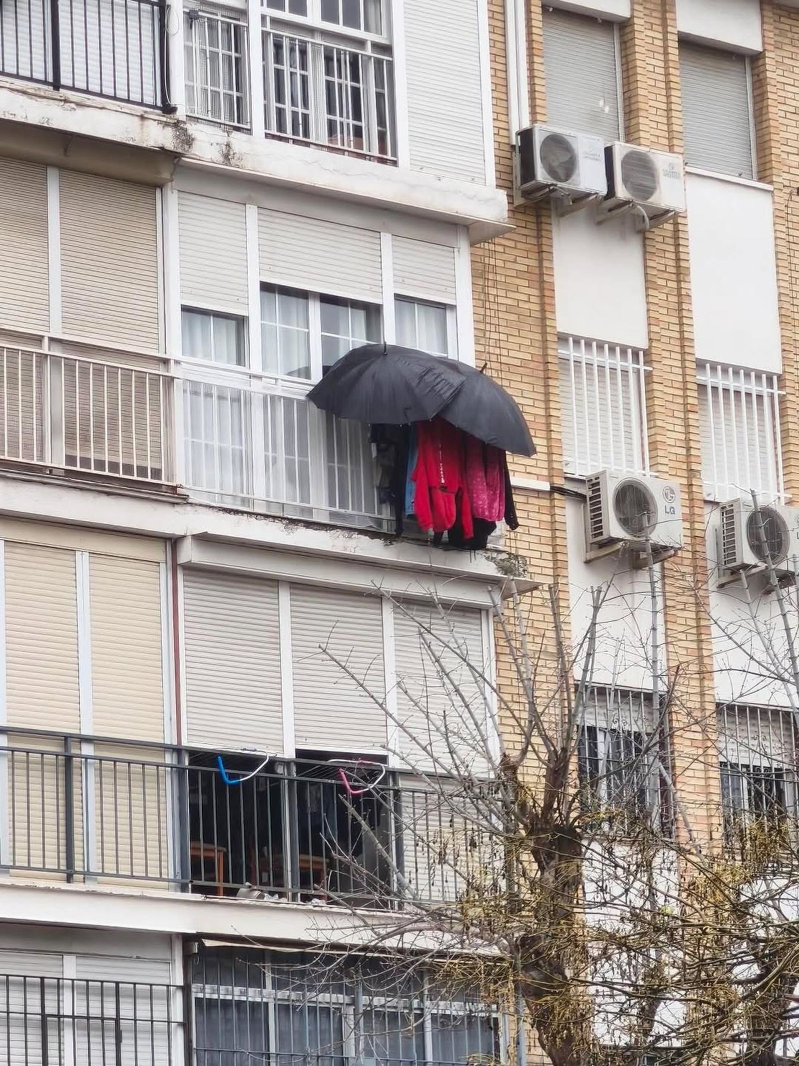 Destreza con paraguas para evitar que la ropa se moje en los balcones de Sevilla
