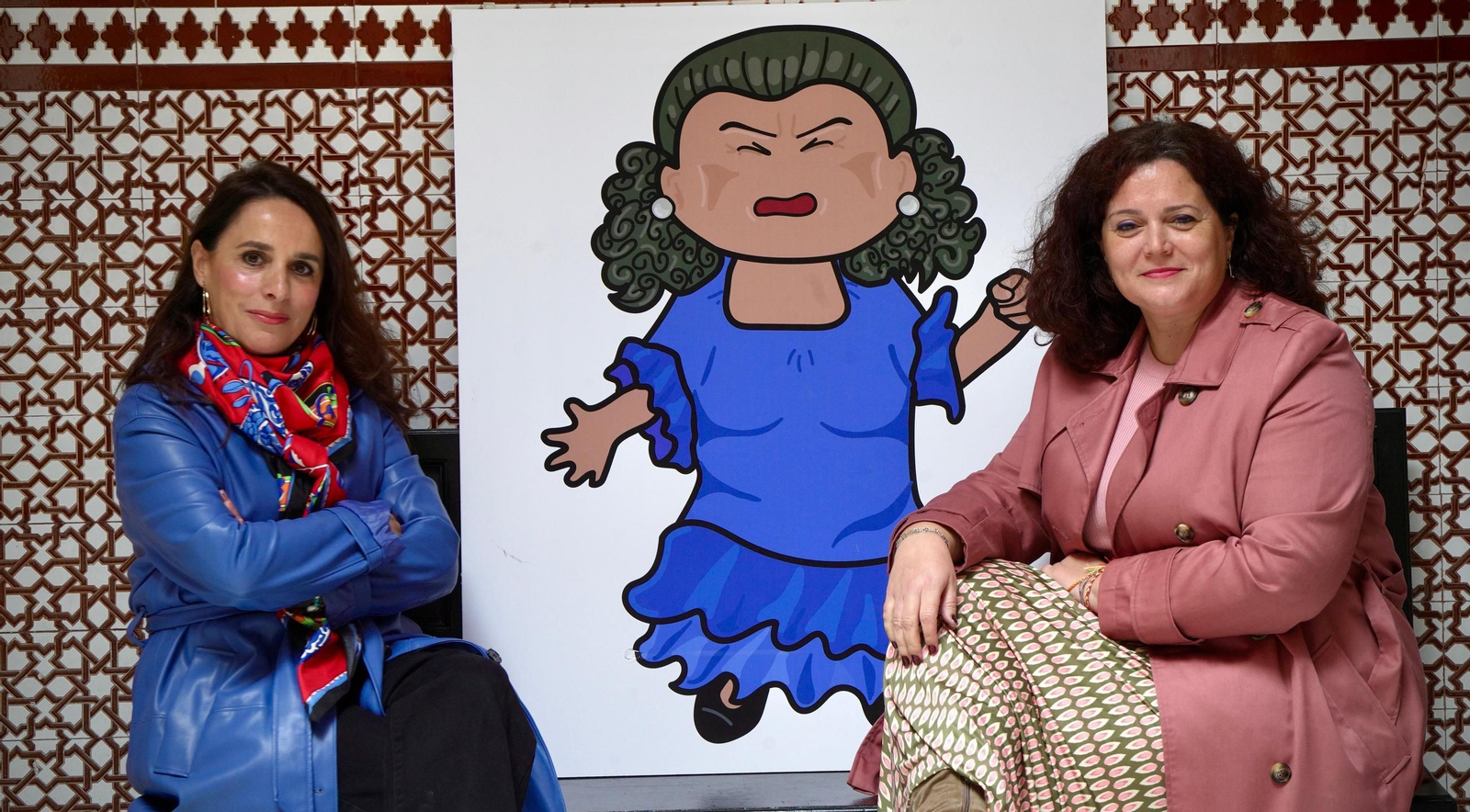 Patricia Noelia Moreno y Raquel Huertas posan junto a la ilustración de La Paquera, una de las artistas que aparecen en el libro.