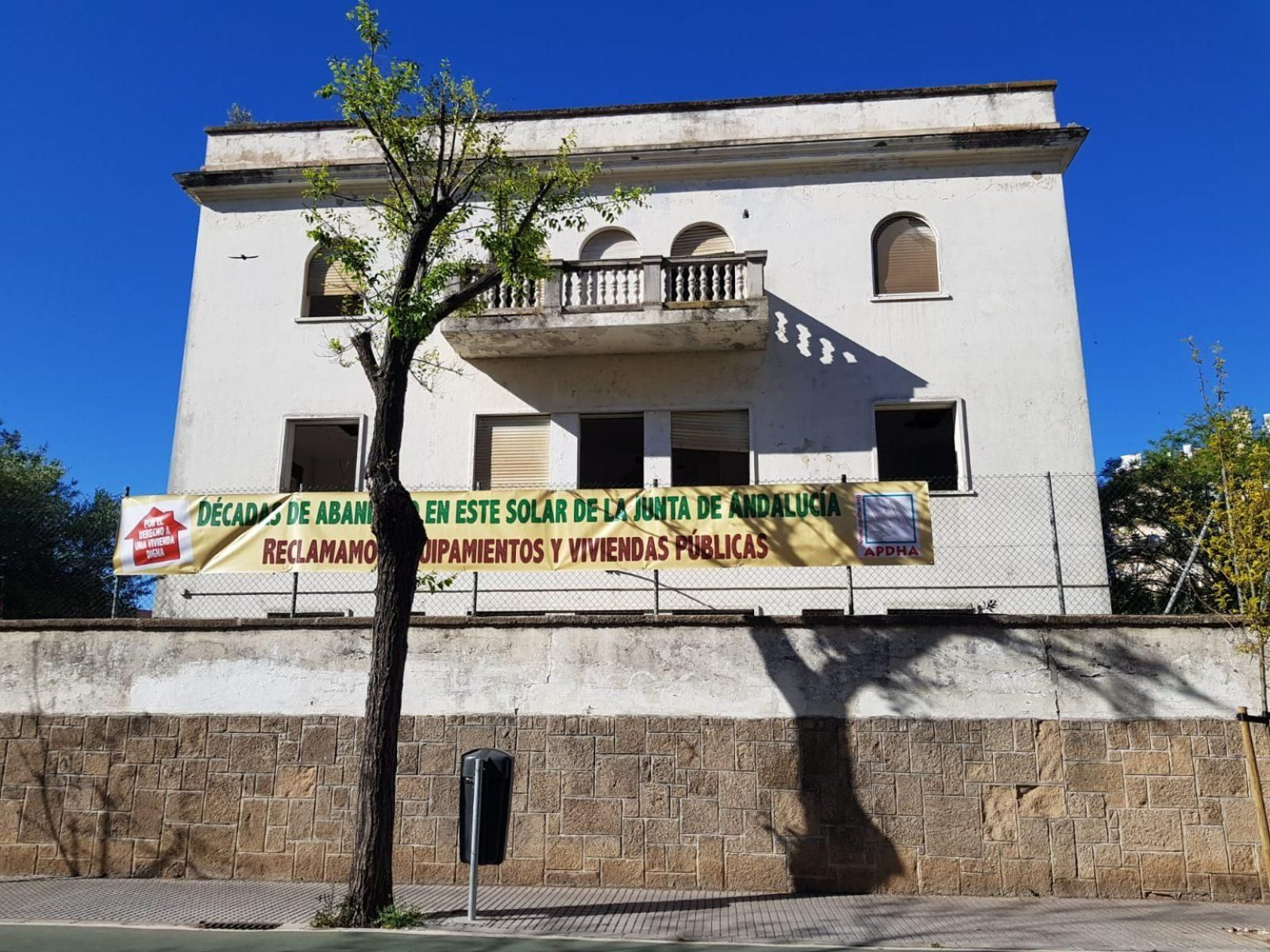 Una imagen de edificio abandonado y la pancarta de la APDHA.