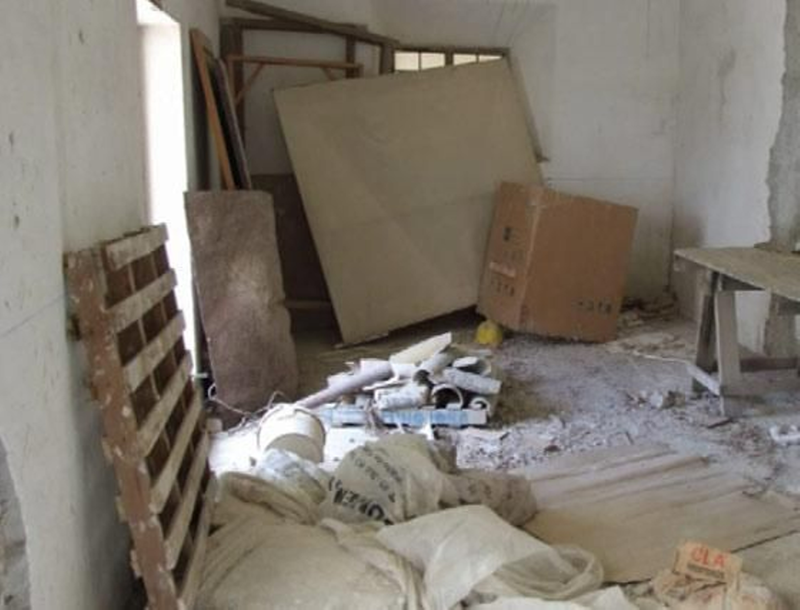 Una zona interior en obras, con cartones, maderas y materiales por el suelo.