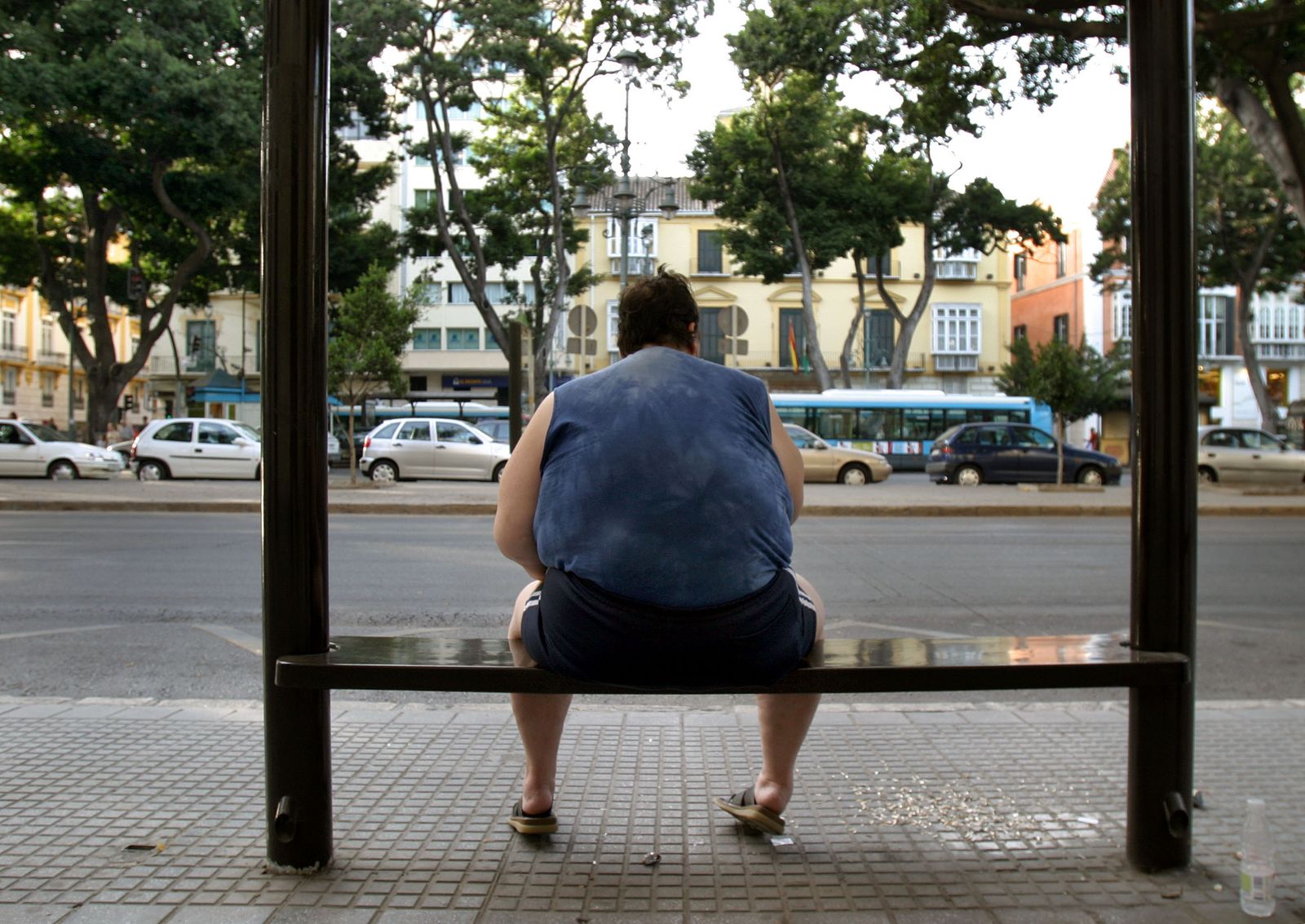 Un hombre obeso sentado en una parada de autobús.