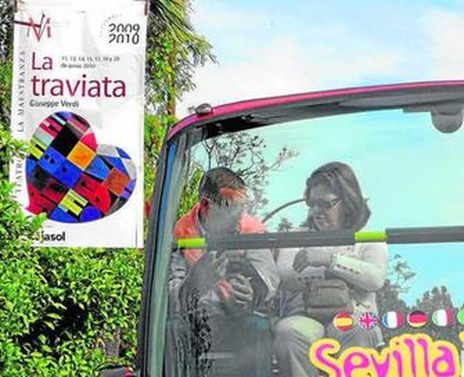 Dos viajeros de un bus turístico junto a un cartel de 'La Traviata'.