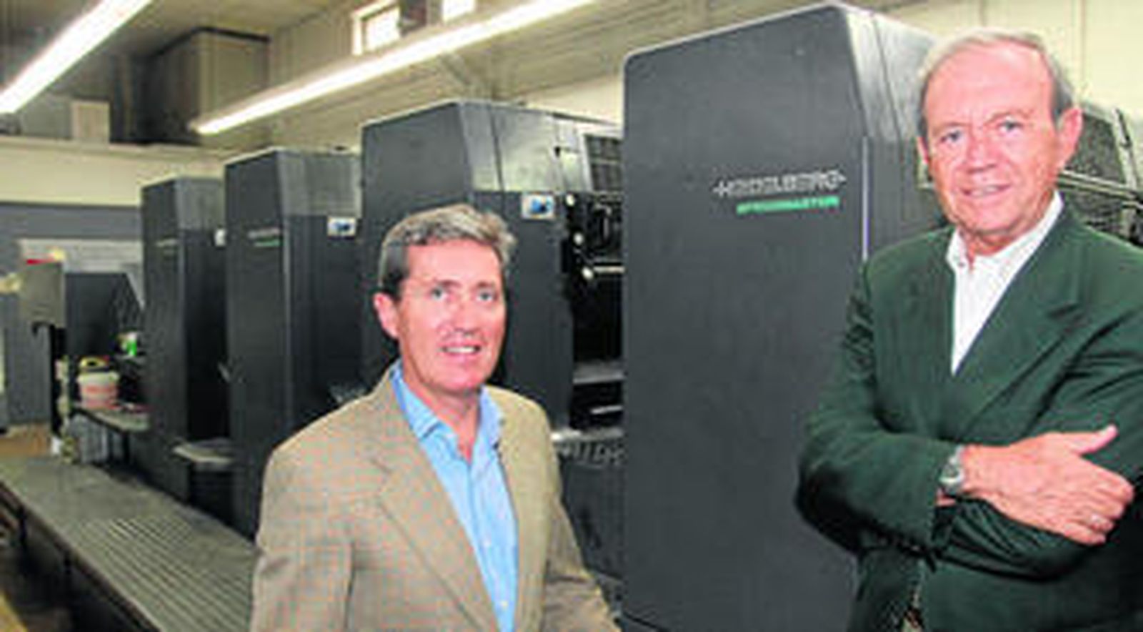 Los propietarios de Gráficas Urania, Esteban y Juan Andrés Bueno, posan junto a la imprenta Heidelberg, una de las insignias de la empresa.