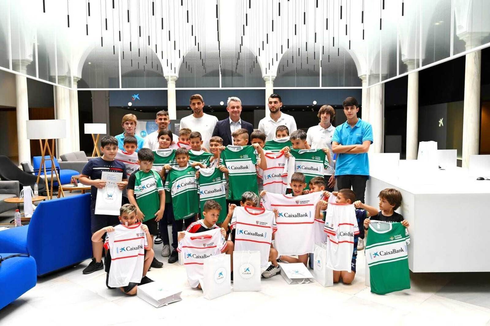 Ignacio Blasco, director comercial de CaixaBank en Sevilla junto a los jugadores de Sevilla y Betis y los niños de Alalá.