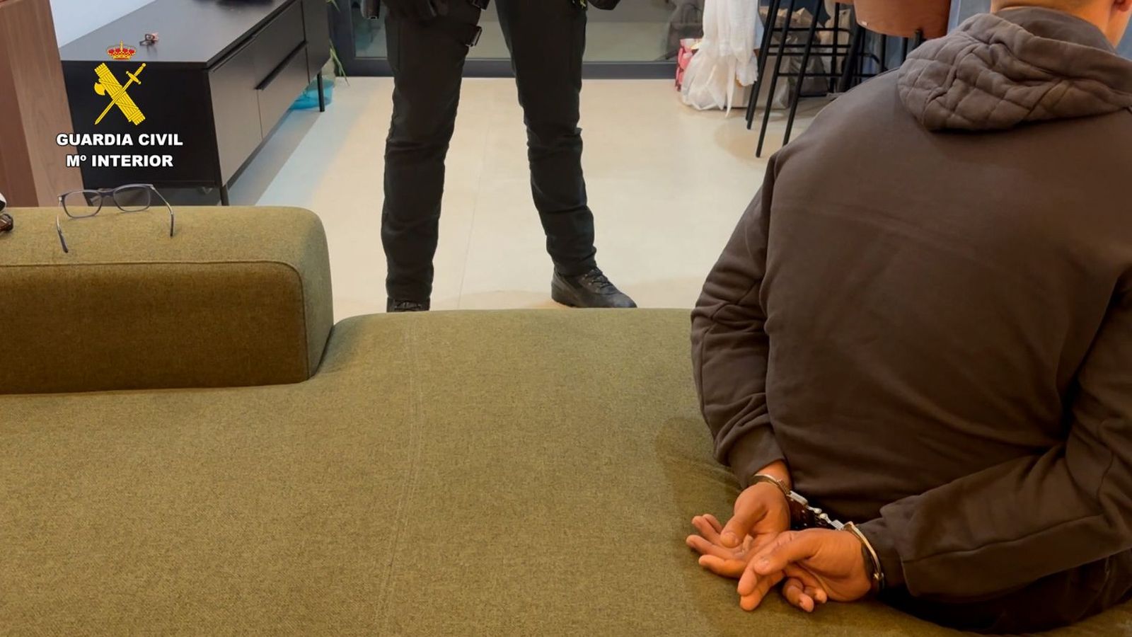 Uno de los detenidos, esposado y custodiado por un agente de la Guardia Civil.