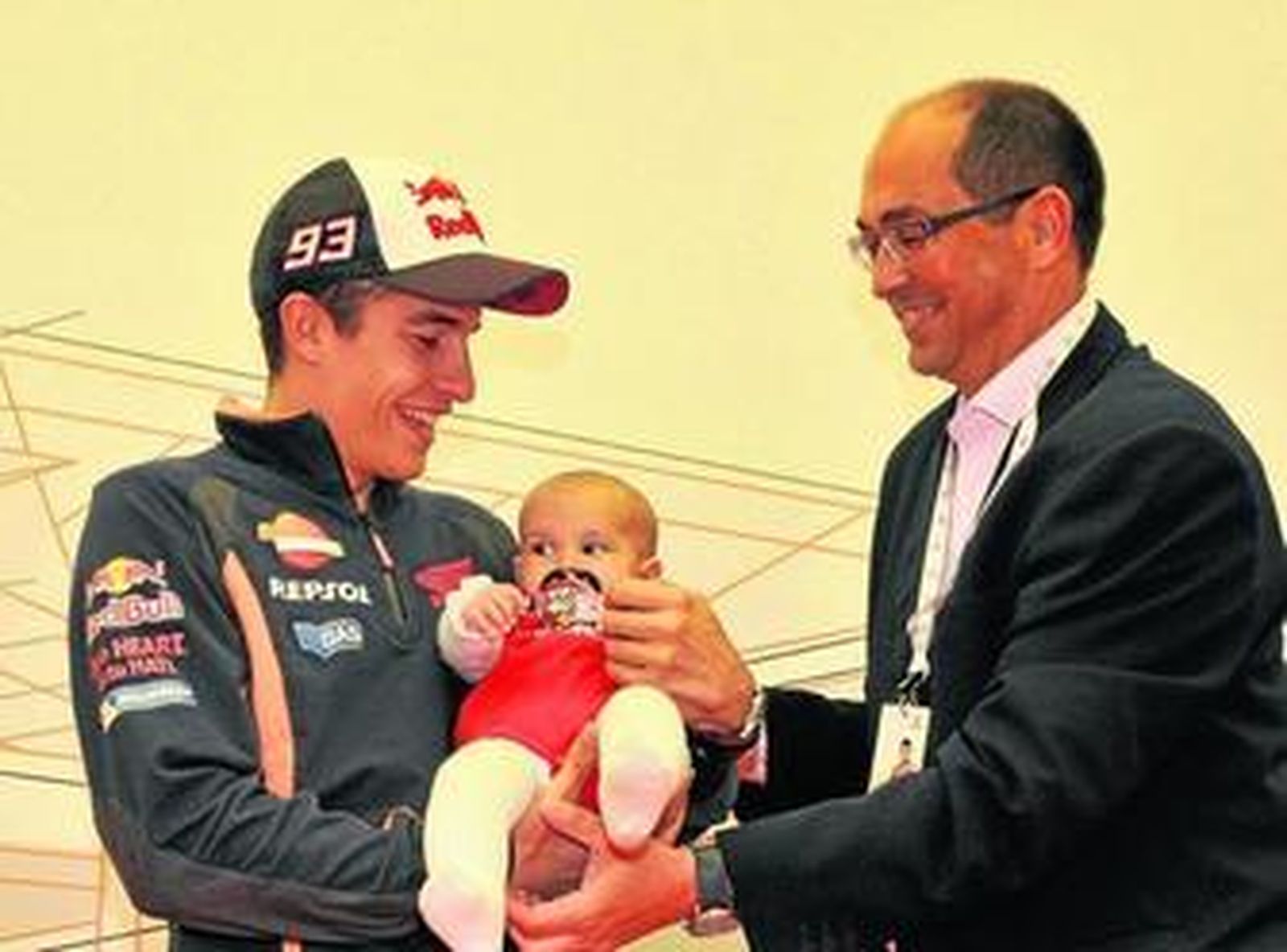 El bicampeón de MotoGP sostiene a una bebé en sus brazos, junto al alcalde de Villamartín.