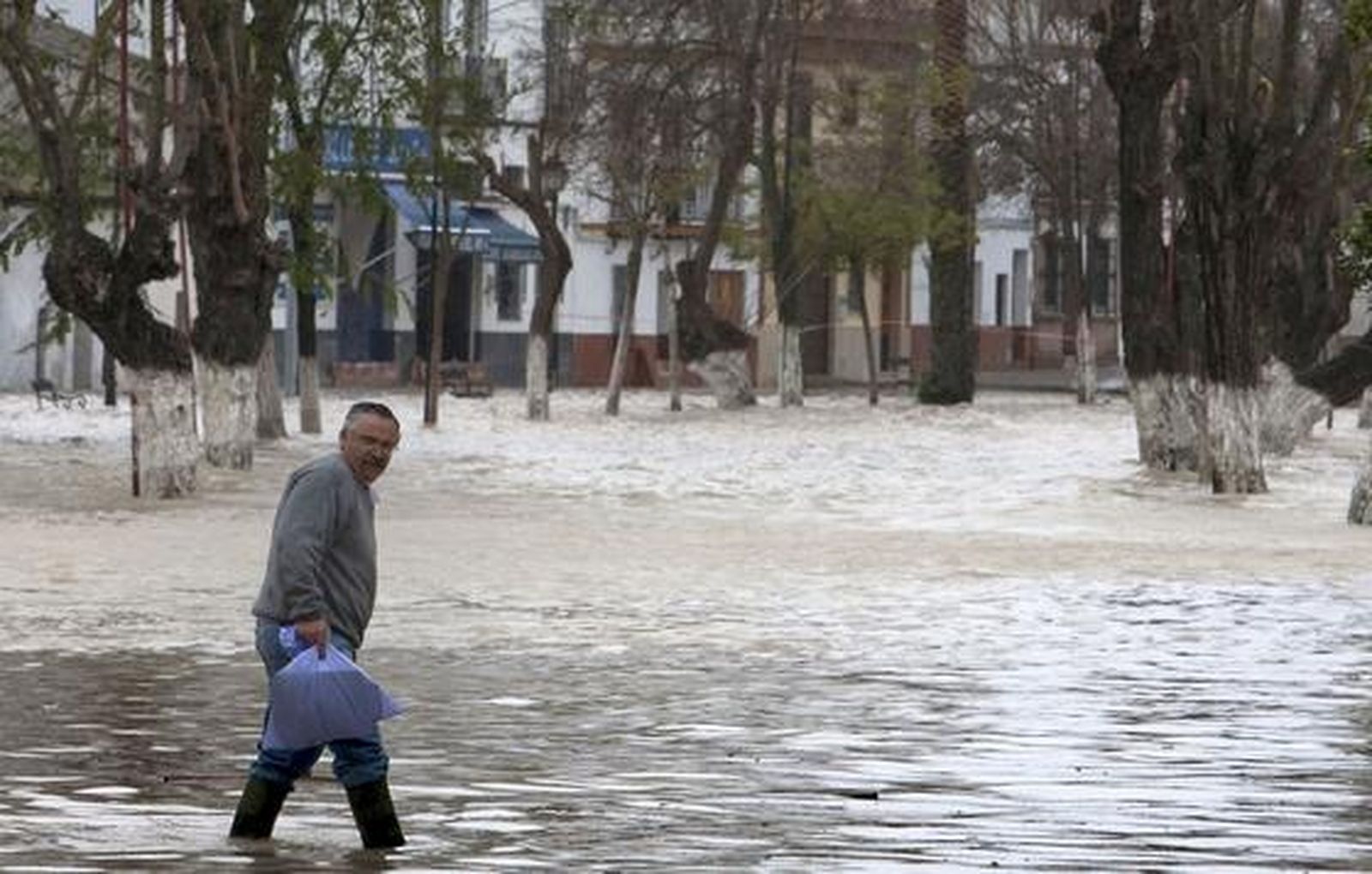 Un hombre sostiene una bolsa y anda sobre el agua que inunda Lora del Río.

Foto: Agencias