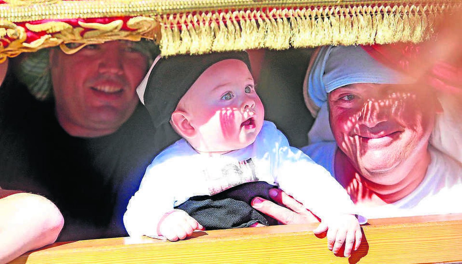 Un pequeño, asido por uno de sus mayores, asoma por los respiraderos del paso de misterio de la Hermandad de la Clemencia