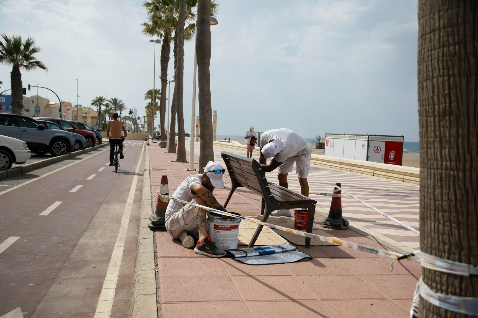 Operarios trabajan pintando un banco en el Paseo Marítimo de Almería capital.