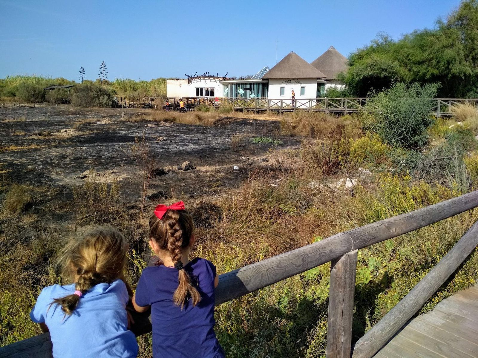 Dos niñas observando ayer por la mañana los daños provocados por el incendio en el centro El Camaleón y el cordón dunar de Chipiona.