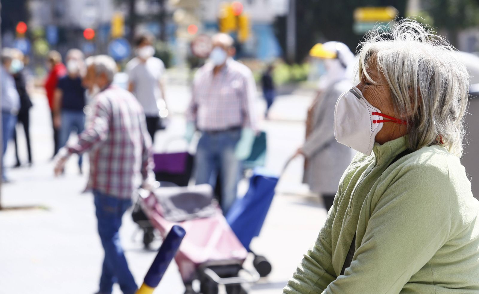 Una mujer con mascarilla hace cola a la puerta de un supermercado.