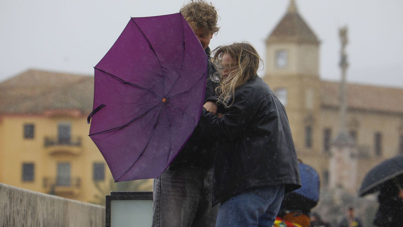 Dos personas sujetan un paraguas frente al viento.