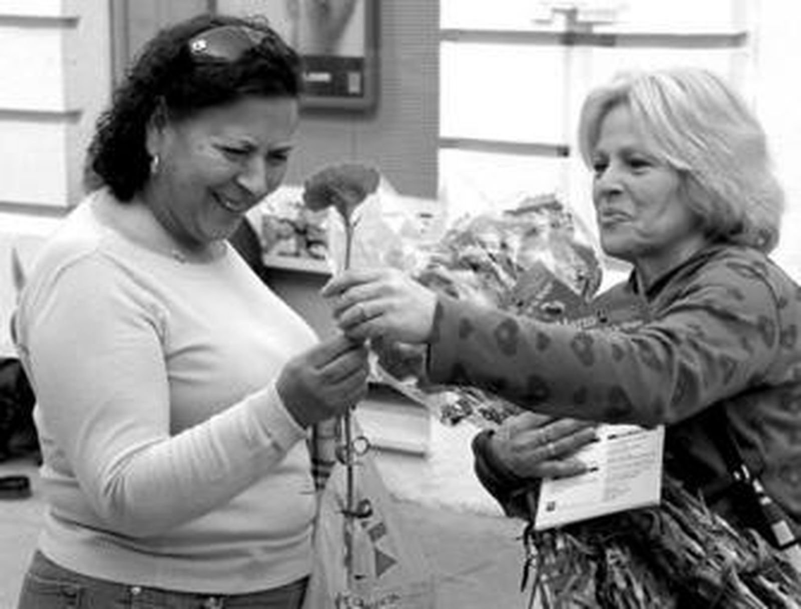Una de las socias de Asocum entrega un clavel a una mujer en la calle La Vega.