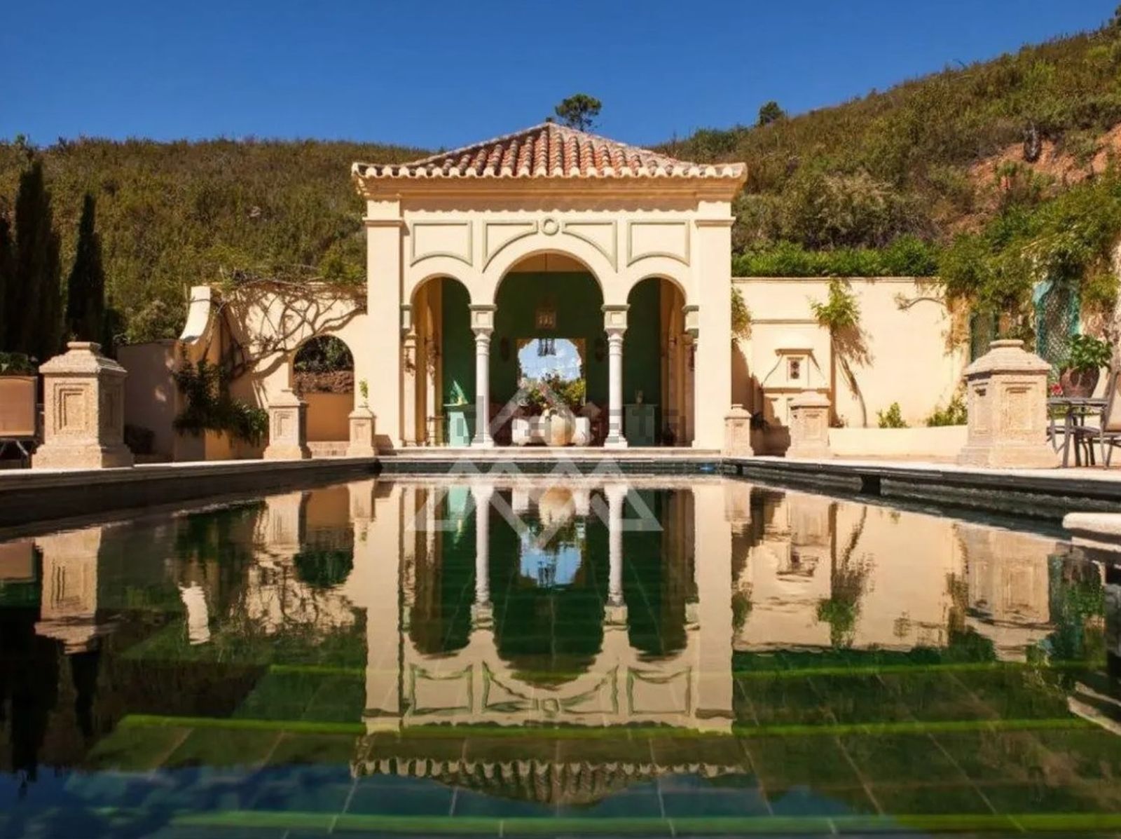 Patio central de la finca, eje arquitectónico de la vivienda, rodeado por arcos de piedra y reflejado en el estanque ornamental.