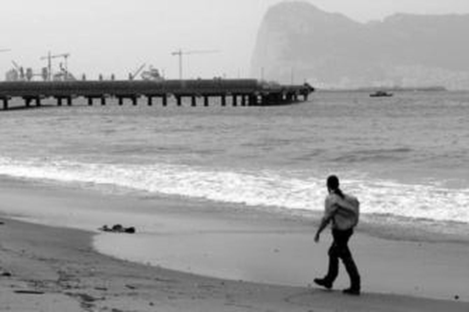 Un técnico de la Junta inspecciona la costa de San Roque tras el vertido ocurrido en el pantalán de la refinería, al fondo.