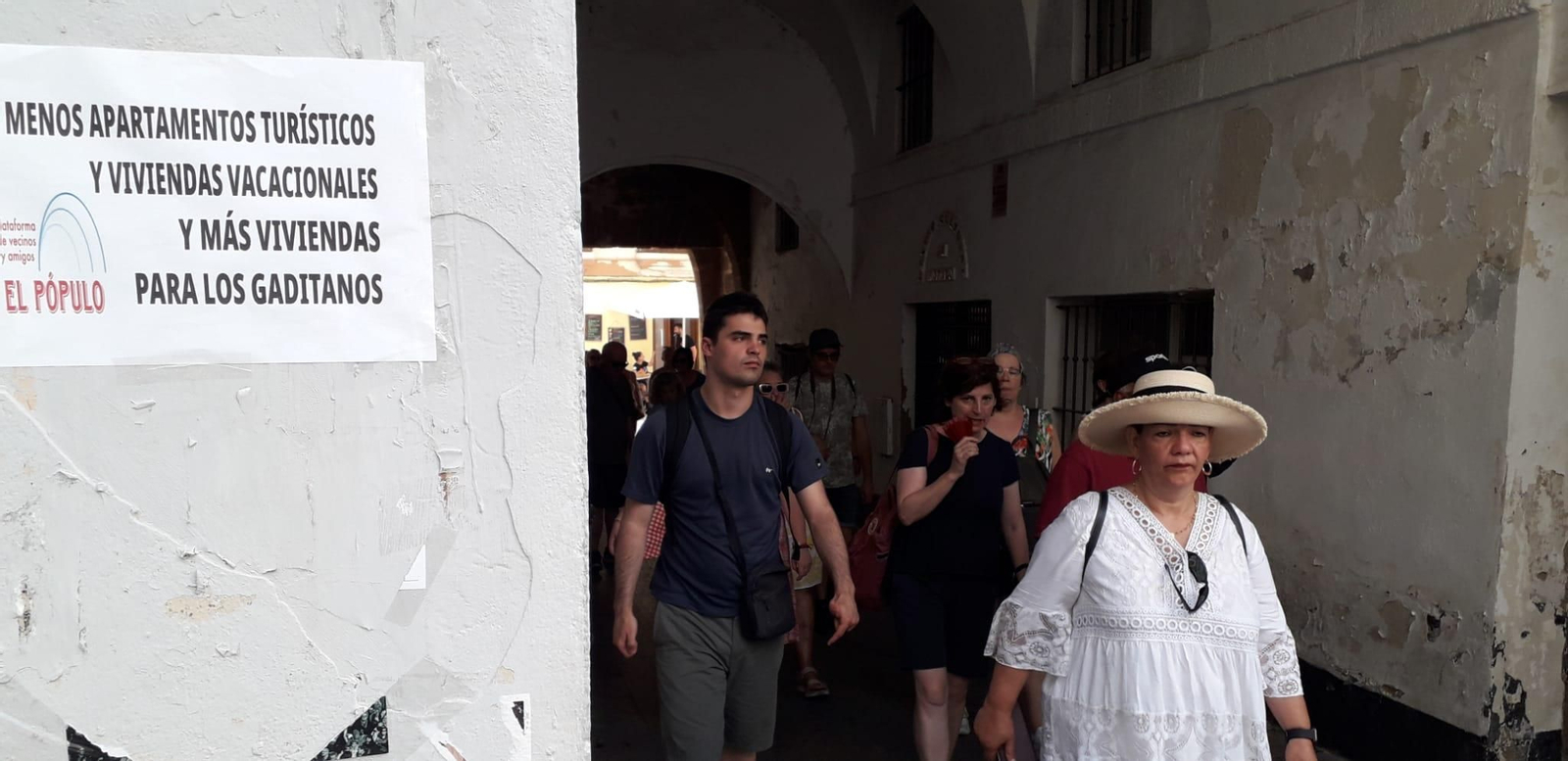 Turistas, visitando el barrio de El Pópulo, una mañana de julio, ante un cartel de la plataforma vecinal contra la turistificación. /