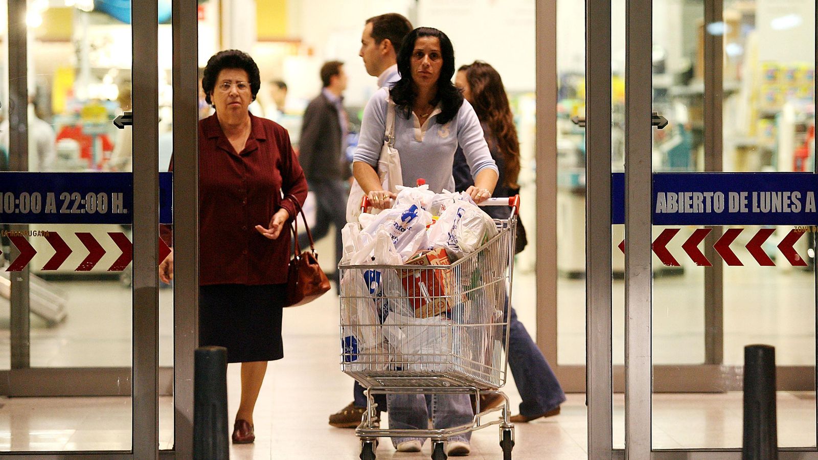 Una mujer sale de un supermercado con el carro de la compra