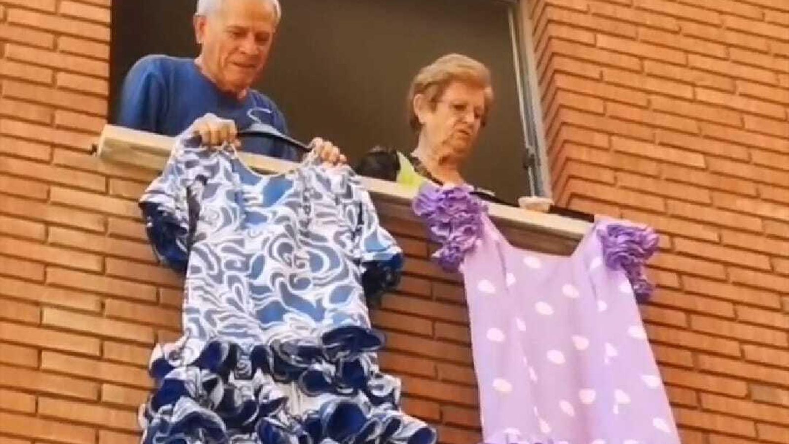 Dos vecinos de Córdoba muestran un par de trajes de flamenca en su ventana.