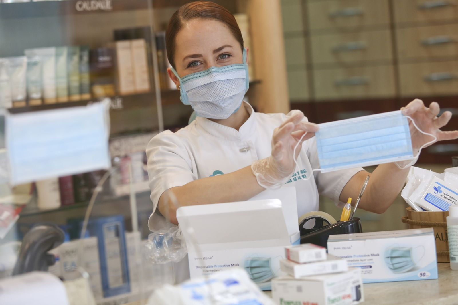 Una empleada de una farmacia muestra una mascarilla quirúrgica.