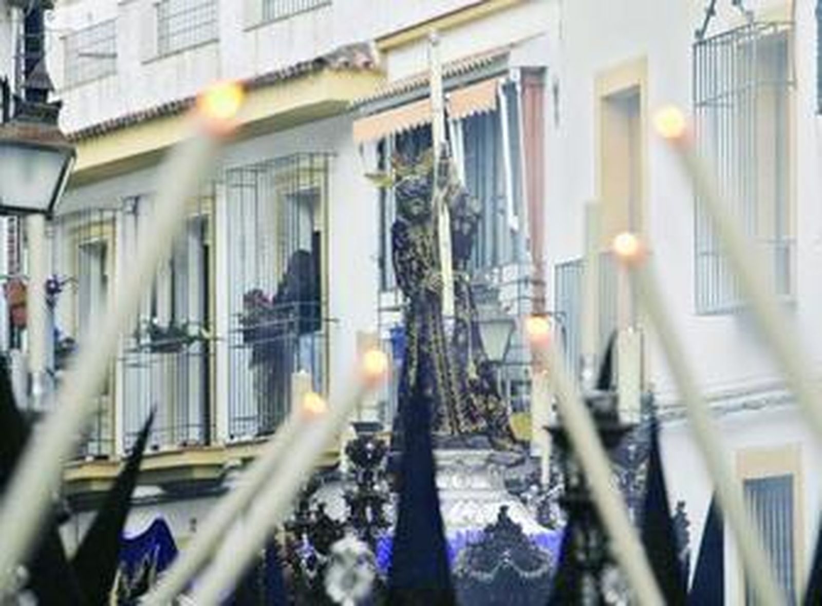Jesús Nazareno, portando una cruz plateada, alumbrado por las velas de los penitentes.