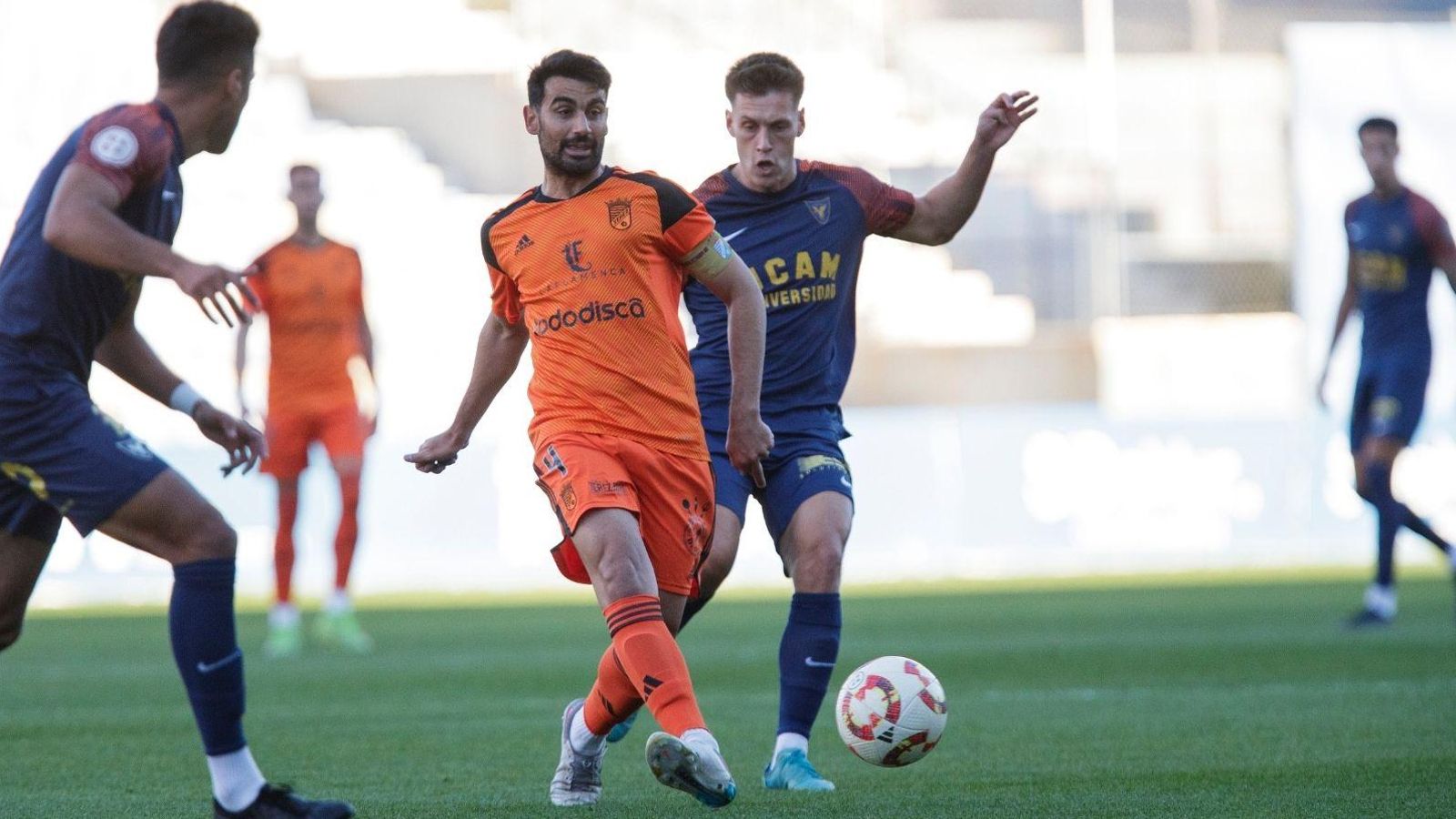 Adri Rodríguez golpea el balón perseguido por un jugador del UCAM.