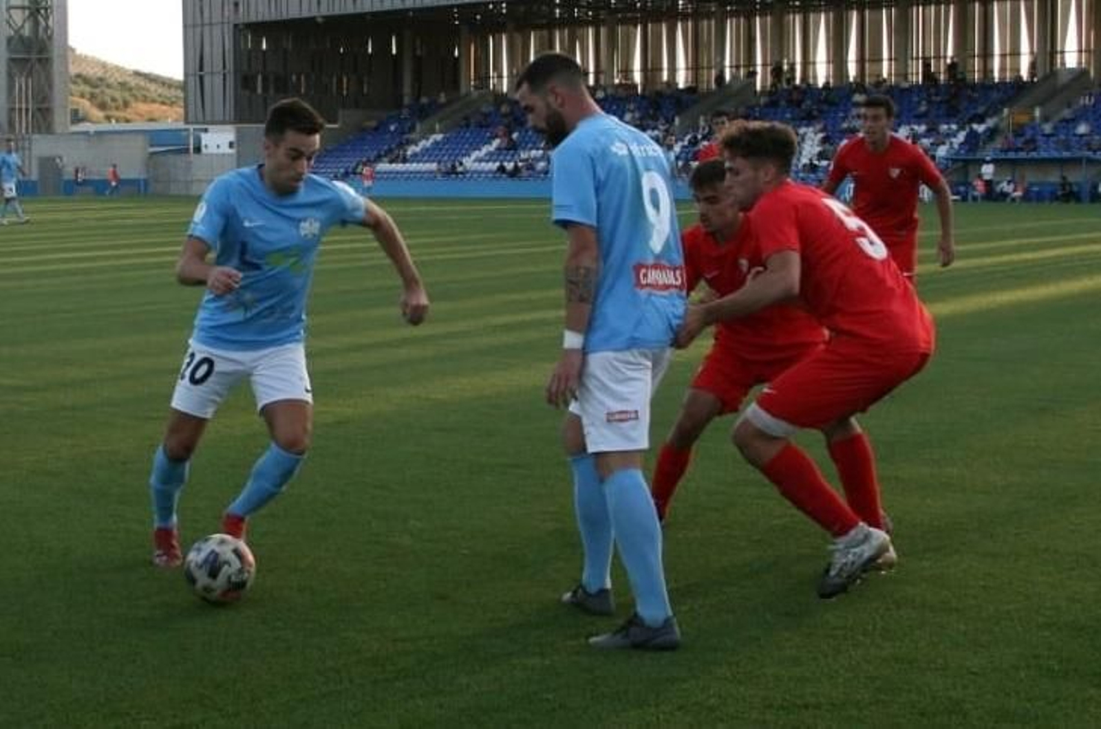 Mario Sánchez intenta esquivar la presión de dos rivales ante la mirada de Juan Delgado.