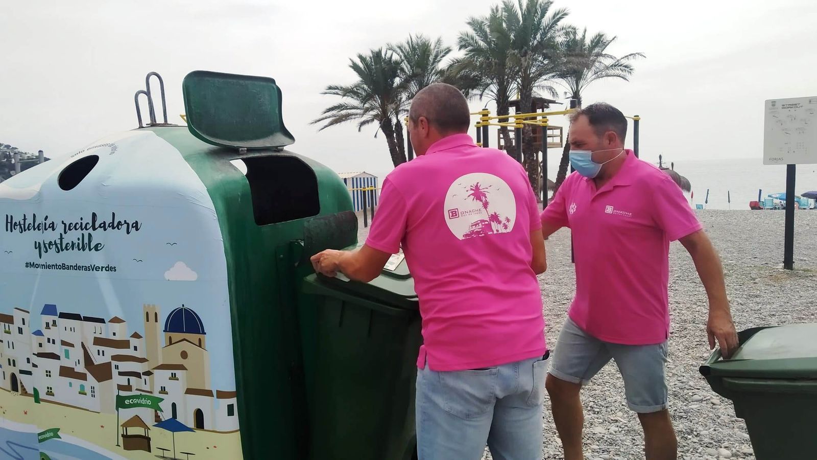 Imágen de archivo de dos personas de una establecimiento tirando botellas de vidrio al contenedor verde