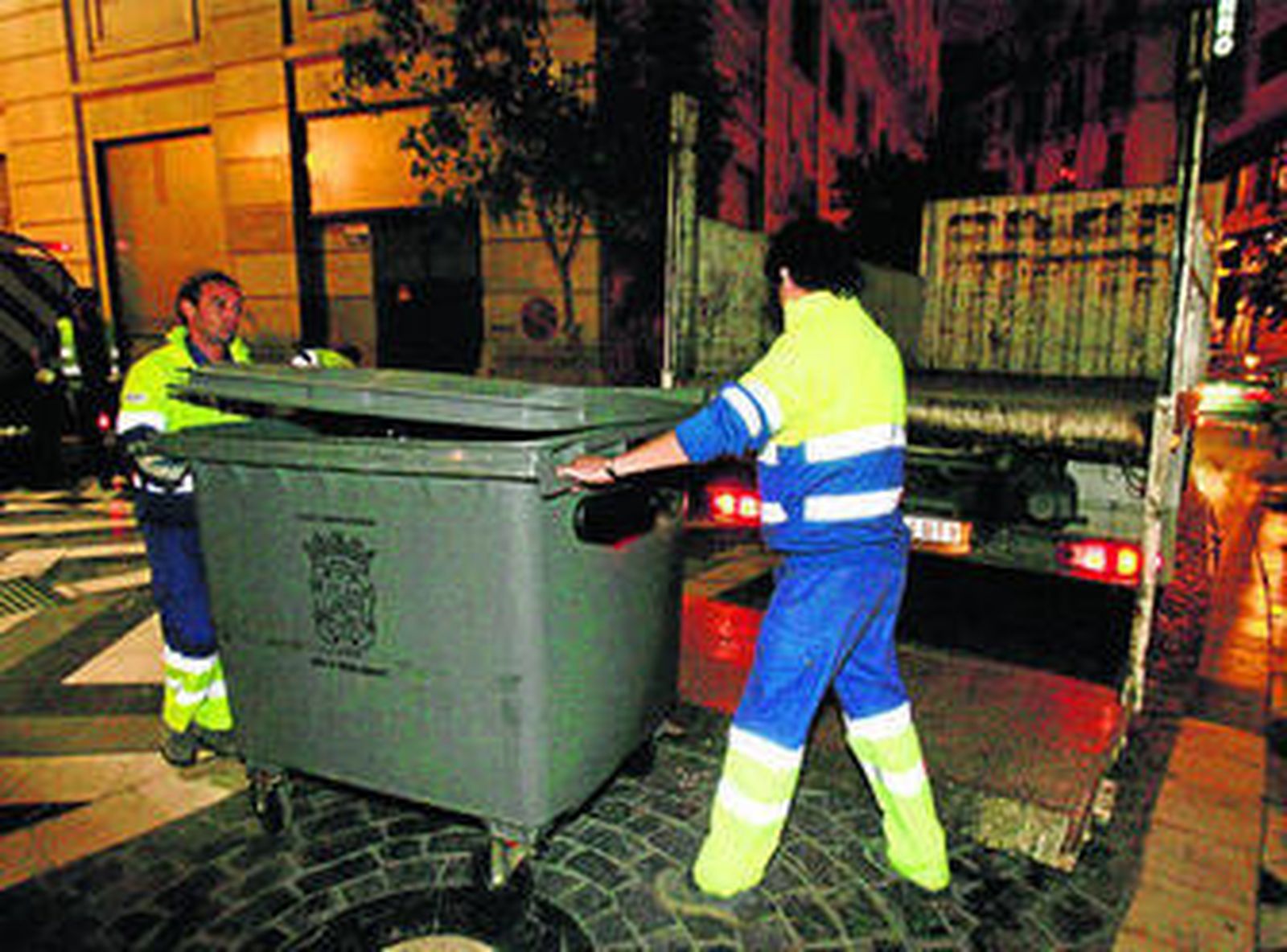 Dos operarios recogen un contenedor de basura del centro de la capital.