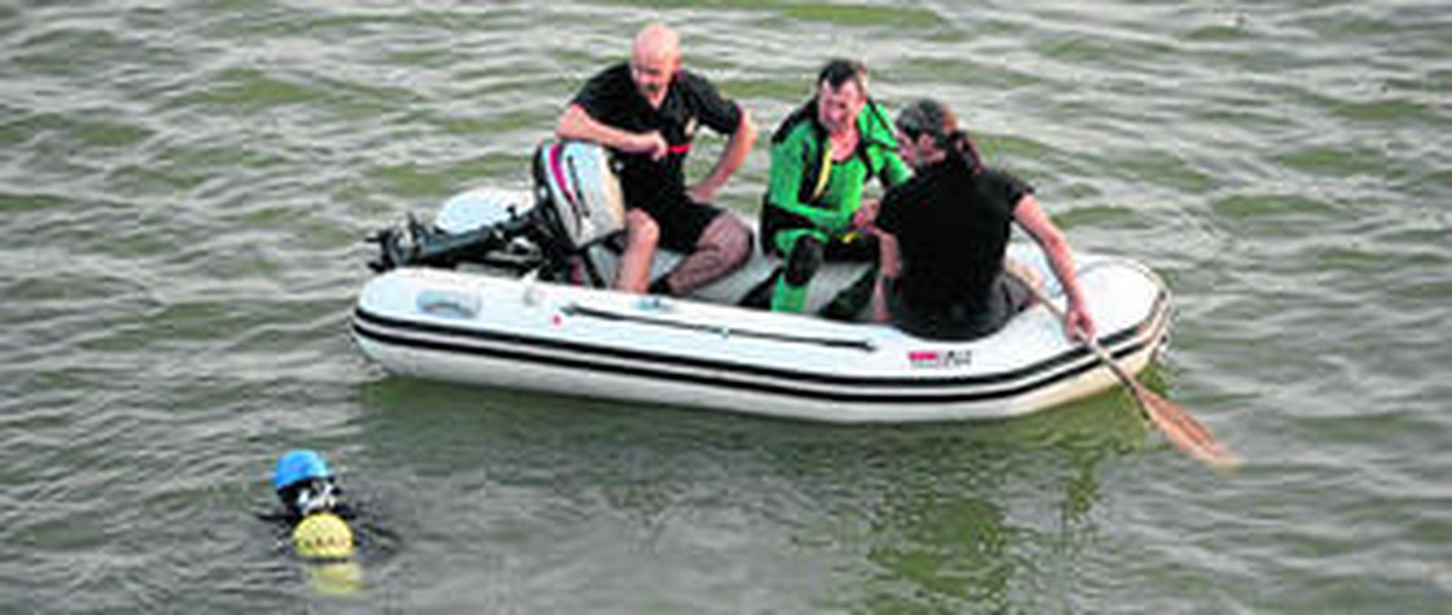 Uno de los buzos de la Guardia Civil se sumerge en el río mientras su compañero y dos bomberos le apoyan desde una barca.