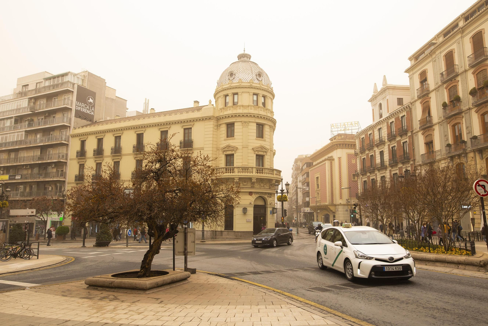 Varios coches circulan por el centro de la capital con la calima de fondo.