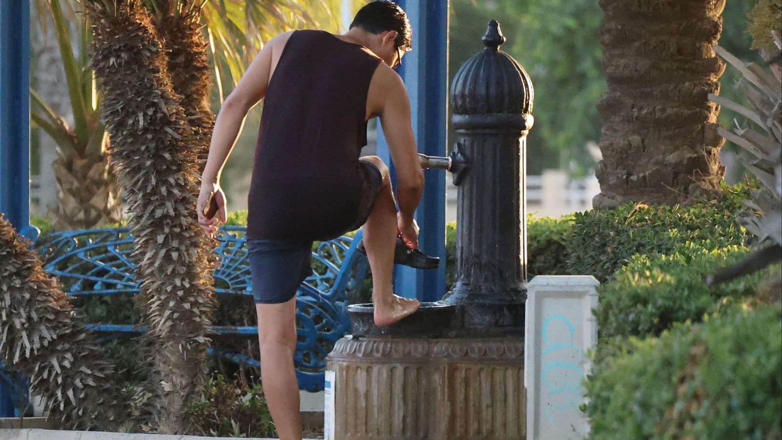 Un joven lavándose los pies en una fuente destinada para beber.