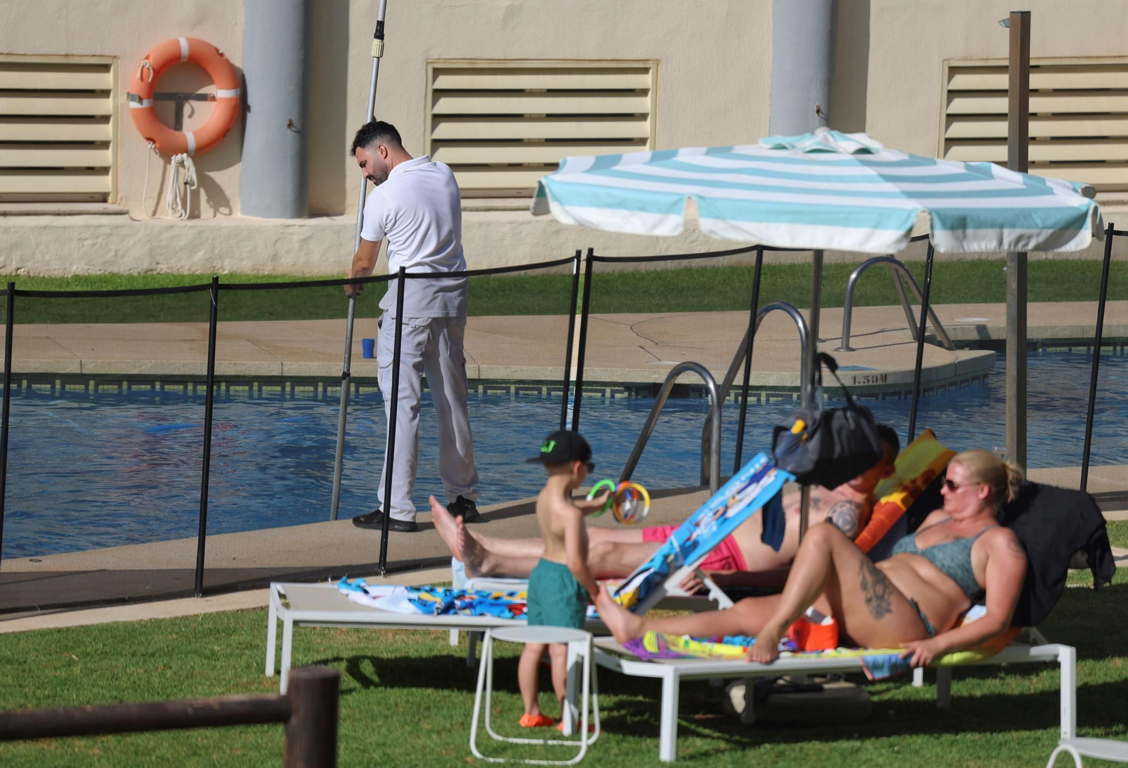 Un trabajador limpia una piscina en un hotel de la provincia junto a turistas.