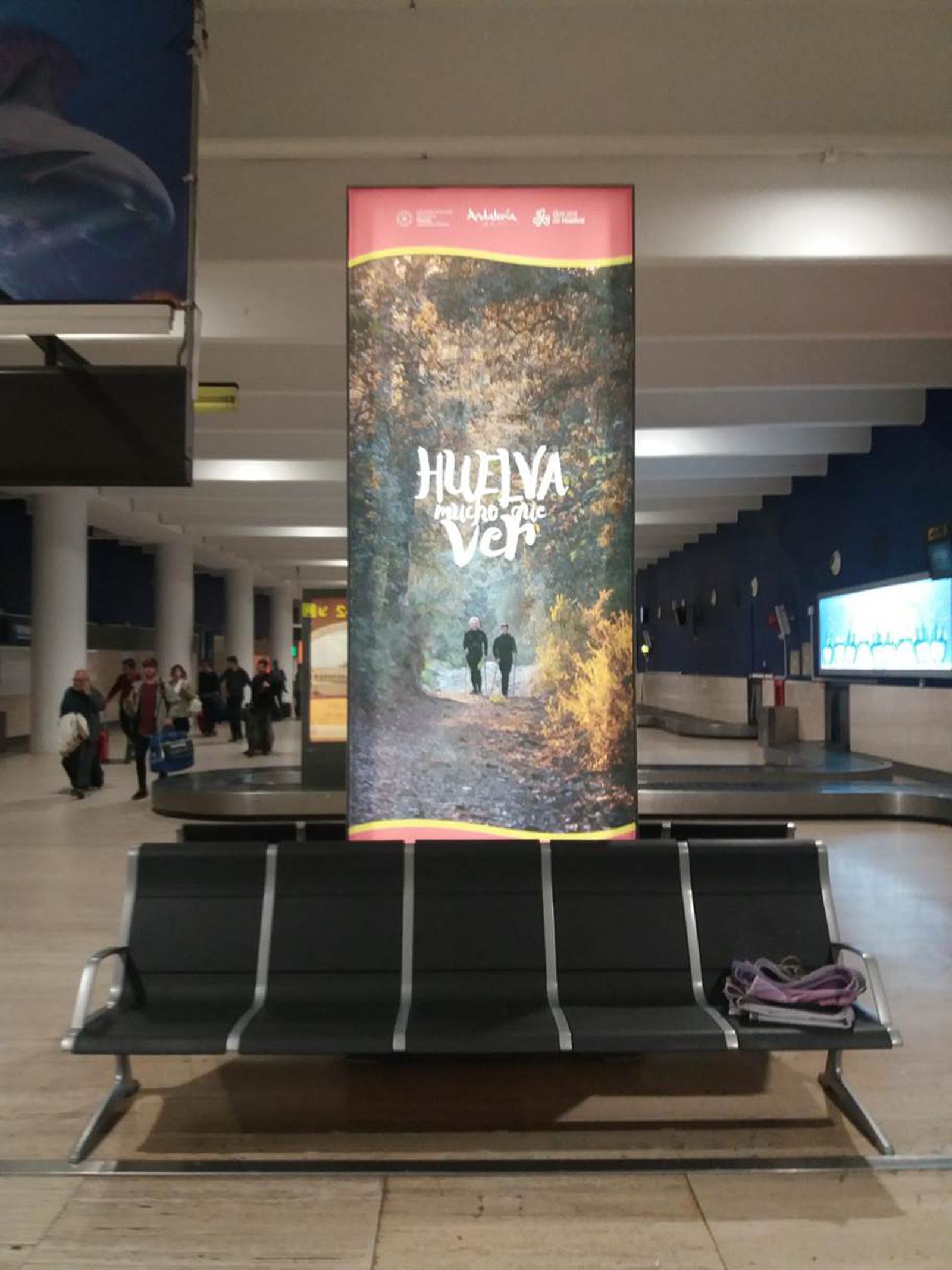 Cartel con una imagen de senderismo en la Sierra onubense en la zona de recogida de equipajes del aeropuerto de Sevilla.