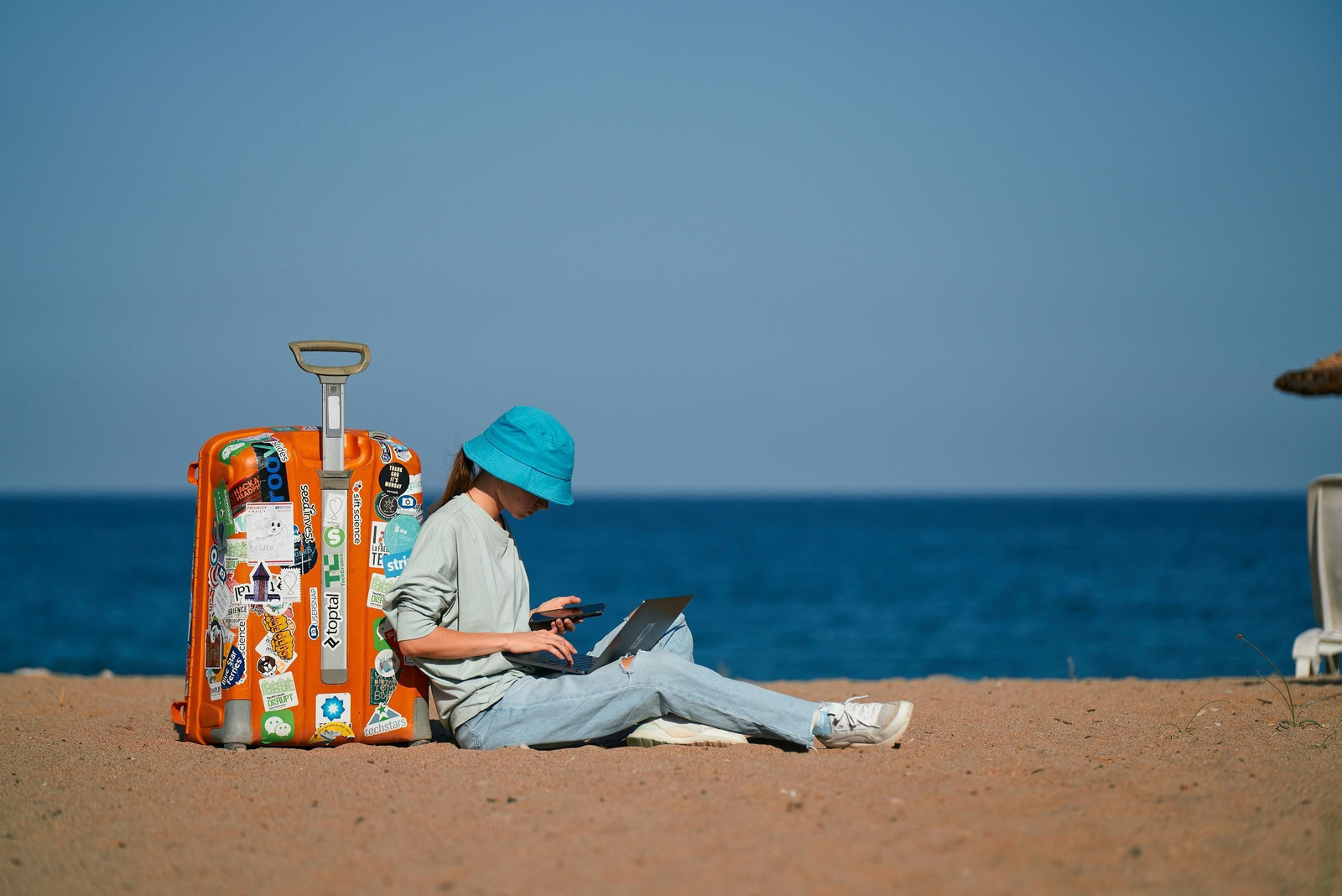 Una joven se apoya en su maleta para teletrabajar desde la playa.